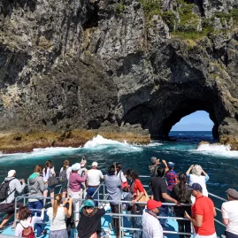 Tourists on a boat approaching the famous Hole in the Rock at Motukokako Island, Bay of Islands, New Zealand.