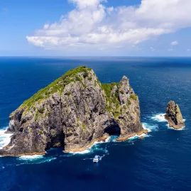 Aerial view of the famous Hole in the Rock at Motukokako Island, Bay of Islands, New Zealand, with a tour boat passing through.