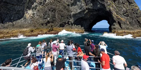 Tourists on a boat approaching the famous Hole in the Rock at Motukokako Island, Bay of Islands, New Zealand.