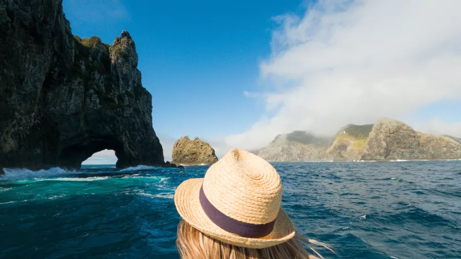 Woman on a boat tour approaching the famous Hole in the Rock at Motukokako Island, Bay of Islands, New Zealand.