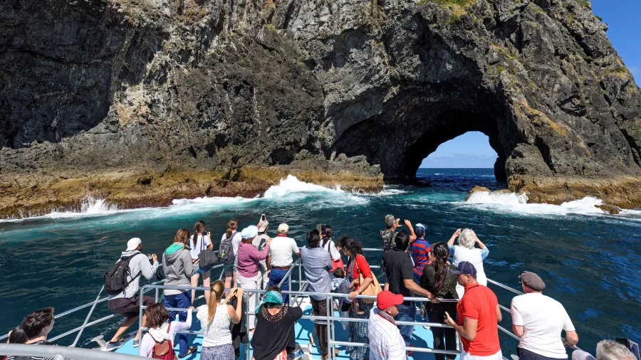 Tourists on a boat approaching the famous Hole in the Rock at Motukokako Island, Bay of Islands, New Zealand.