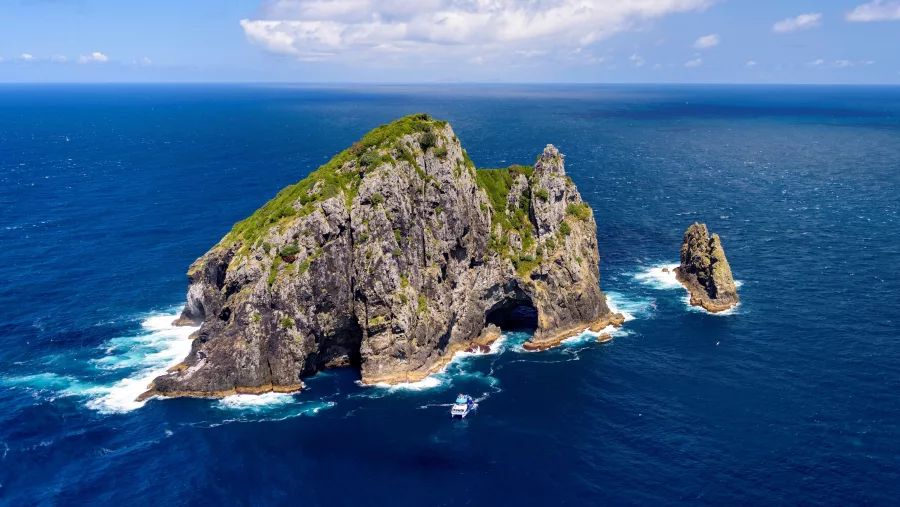 Aerial view of the famous Hole in the Rock at Motukokako Island, Bay of Islands, New Zealand, with a tour boat passing through.