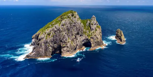Aerial view of the famous Hole in the Rock at Motukokako Island, Bay of Islands, New Zealand, with a tour boat passing through.