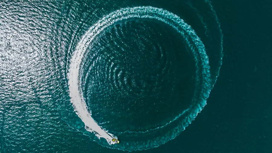 A high-speed boat creating a perfect circular wake pattern on the ocean surface, captured from an aerial view.
