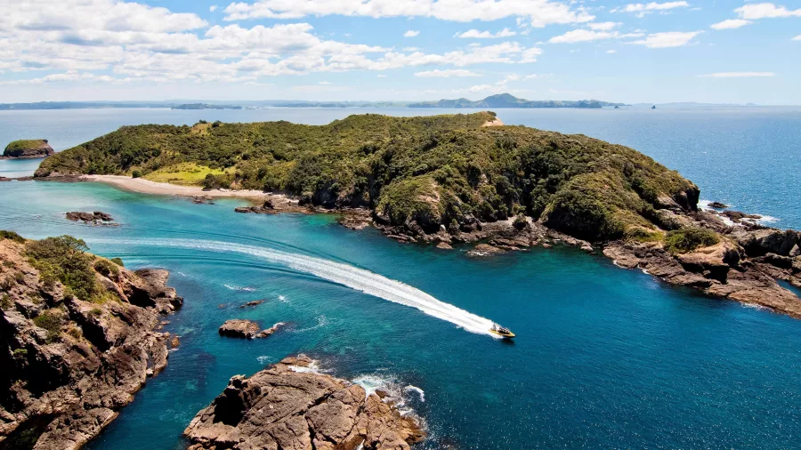 Aerial view of a speedboat cruising through the clear blue waters of the Bay of Islands, New Zealand, surrounded by lush green islands.