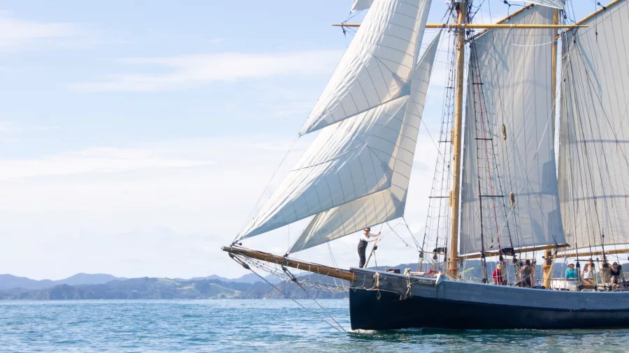A sailor standing on the bowsprit of the R. Tucker Thompson tall ship as it glides through the calm waters of the Bay of Islands.
