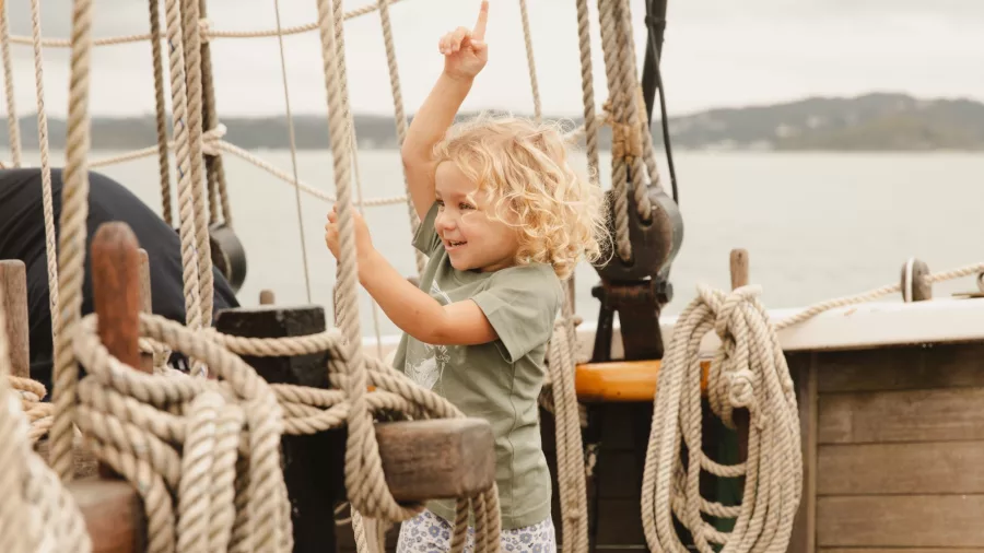 A young child excitedly explores the rigging of the R. Tucker Thompson sailing ship in the Bay of Islands, New Zealand.