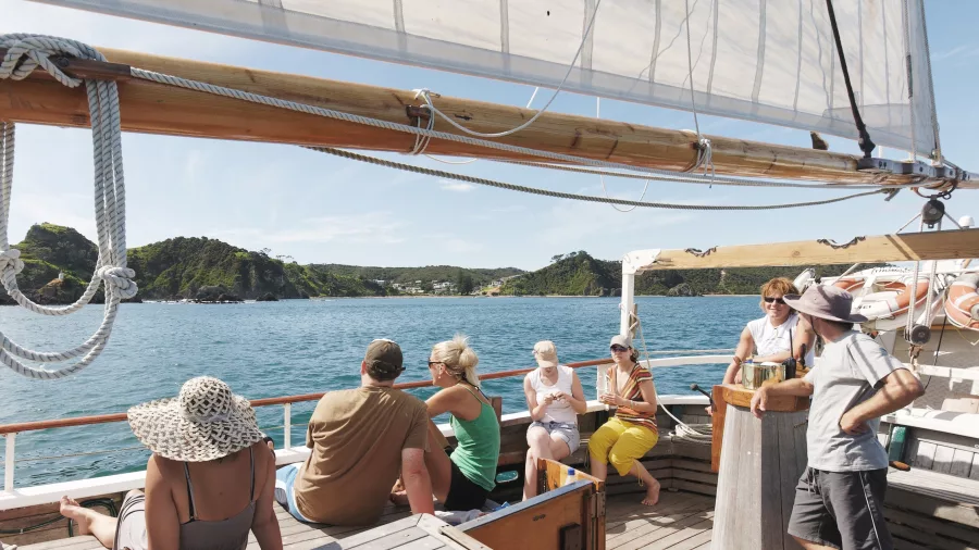 A group of people relaxing on a wooden sailing boat, enjoying the scenic views of the Bay of Islands under a clear sky.