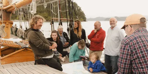 A group of passengers attentively listening to the captain share stories aboard the R. Tucker Thompson.