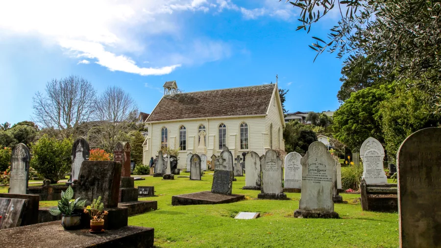 A historic church with a well-preserved graveyard, surrounded by lush greenery under a bright blue sky.