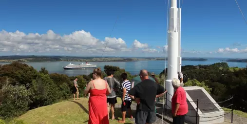 Visitors at Flagstaff Hill enjoy panoramic ocean views, with a historic flagpole and a cruise ship in the distance under a clear blue sky.