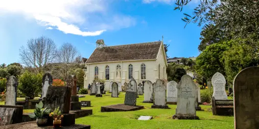 A historic church with a well-preserved graveyard, surrounded by lush greenery under a bright blue sky.