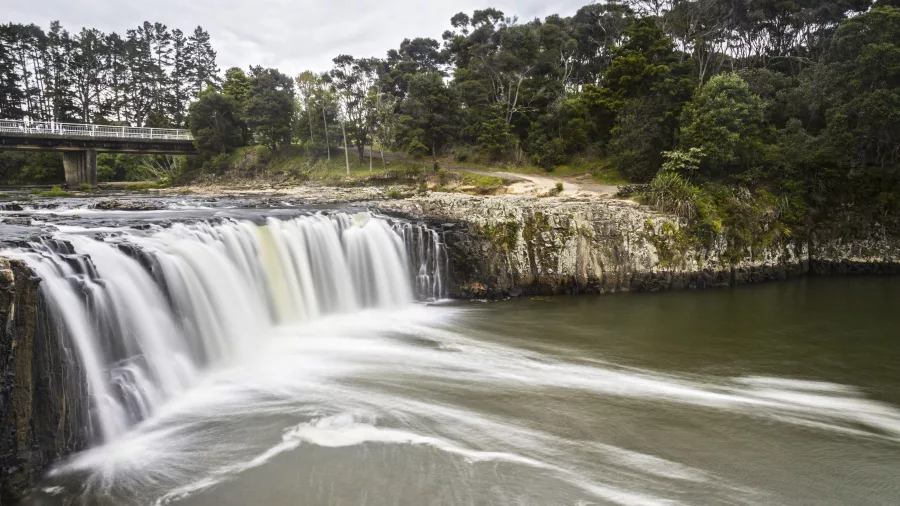 Long exposure photo of Haruru Falls waterfall with surrounding forest and bridge