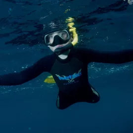 Snorkeller with arms outstretched in deep blue water near Paihia in the Bay of Islands, New Zealand.