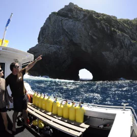 Dive boat near Piercy Island with Hole in the Rock visible as two people look toward the formation in the Bay of Islands