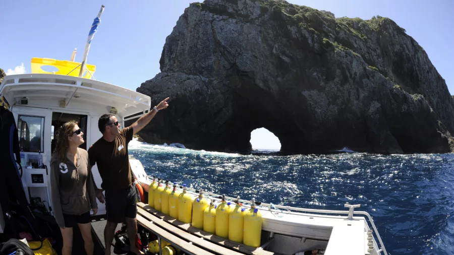 Dive boat near Piercy Island with Hole in the Rock visible as two people look toward the formation in the Bay of Islands