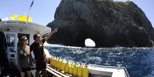 Dive boat near Piercy Island with Hole in the Rock visible as two people look toward the formation in the Bay of Islands