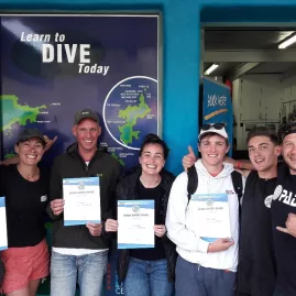 Newly certified PADI Open Water divers holding certificates outside a dive centre in Northland, New Zealand