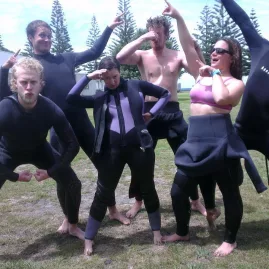 Dive students in wetsuits striking playful poses on the grass during open water training in New Zealand