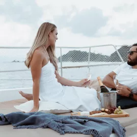 Couple enjoying champagne and a cheese board on the bow lounging pads of a catamaran