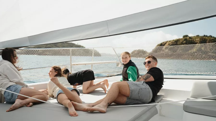 Family relaxing on the foredeck of a catamaran with coastal views in the Bay of Islands