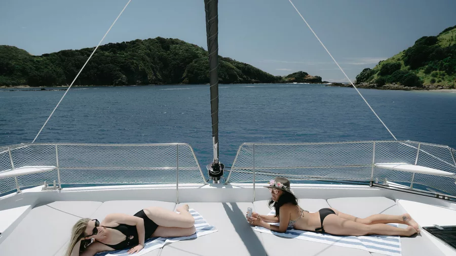 Two women sunbathing on the foredeck of Silver Wave catamaran in the Bay of Islands
