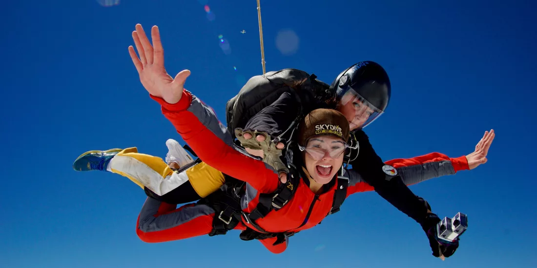 Tandem skydivers in midair freefall with arms outstretched and bright expressions against clear blue sky