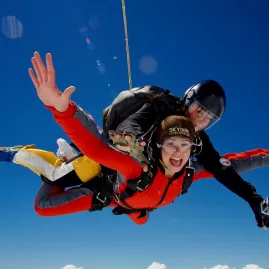 Tandem skydivers in midair freefall with arms outstretched and bright expressions against clear blue sky