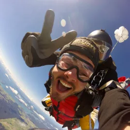 Tandem skydiving selfie at 12000 feet over the Bay of Islands with a smiling jumper flashing a peace sign