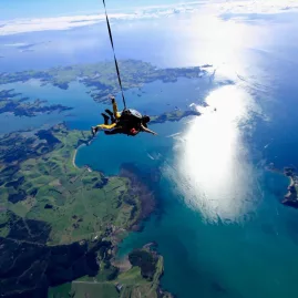 Tandem skydivers at 12000 feet above the Bay of Islands with sunlight reflecting on the ocean