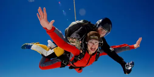 Tandem skydivers in midair freefall with arms outstretched and bright expressions against clear blue sky