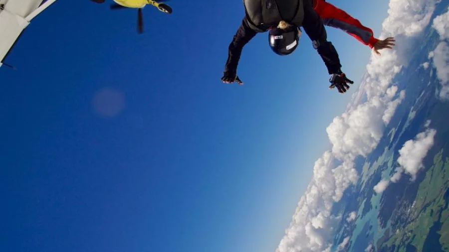 Tandem skydivers exit a yellow plane high above Northland, New Zealand with dramatic cloud and ocean views