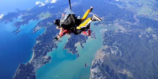 Tandem skydivers descending over the Northland coastline in New Zealand