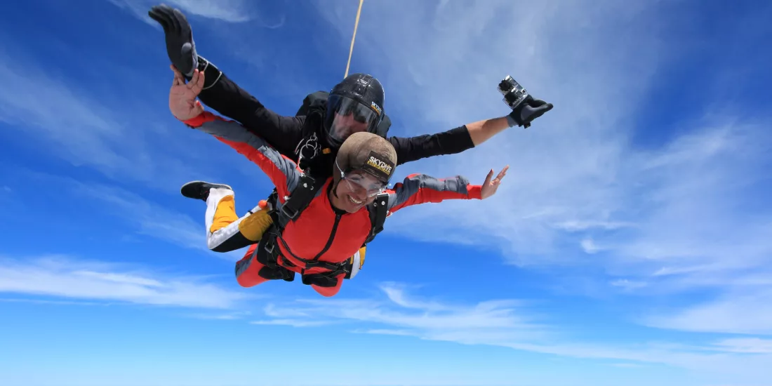 Tandem skydivers freefalling above the clouds with clear blue skies over the Bay of Islands, New Zealand.