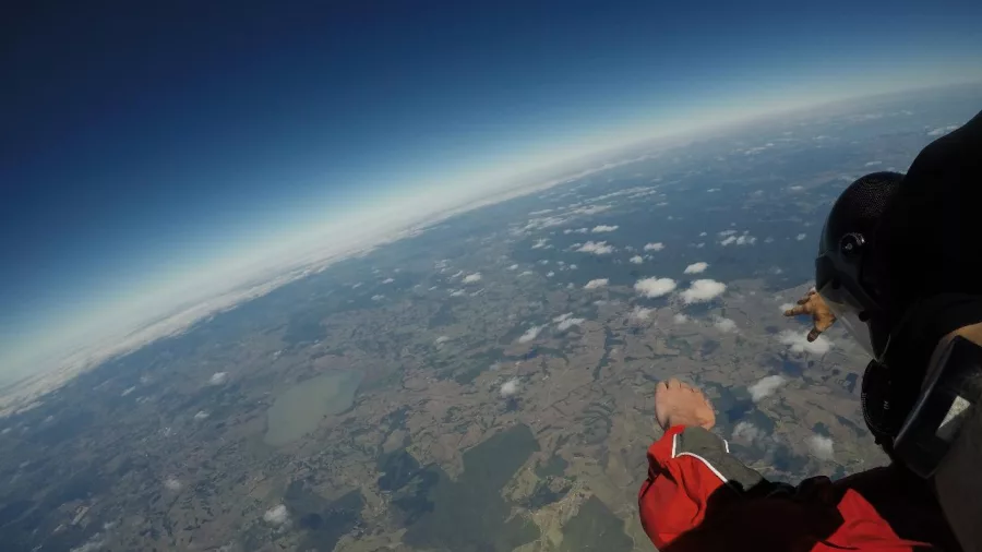 Skydiver in freefall from high altitude with a wide view of the coastline and farmland near the Bay of Islands, New Zealand.