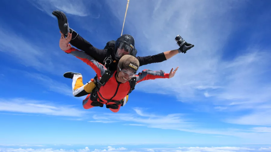 Tandem skydivers freefalling above the clouds with clear blue skies over the Bay of Islands, New Zealand.