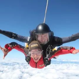 Smiling tandem skydivers freefalling above the clouds with arms outstretched