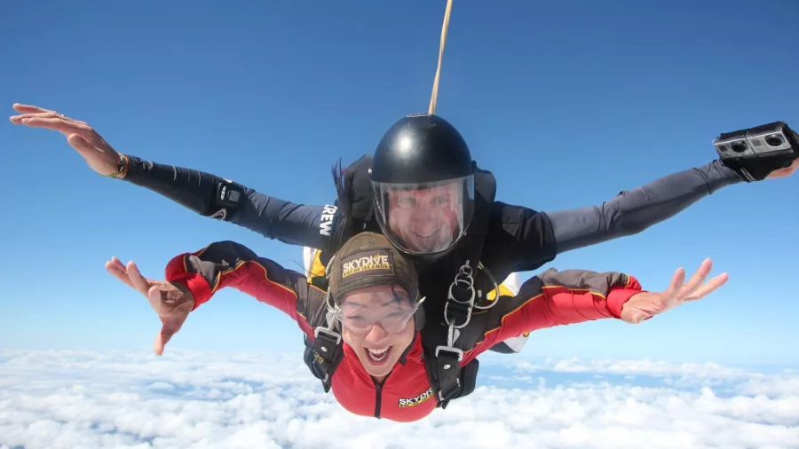 Smiling tandem skydivers freefalling above the clouds with arms outstretched