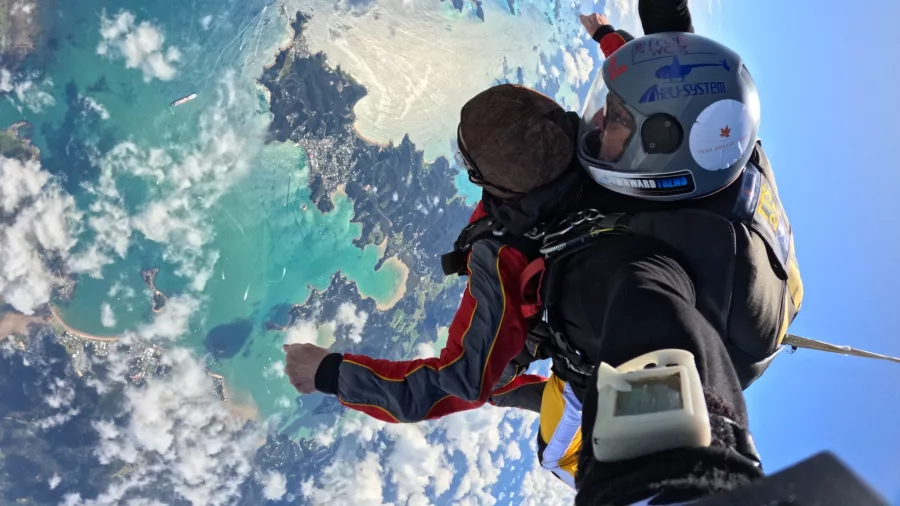 Tandem skydivers freefall above turquoise waters and islands in the Bay of Islands