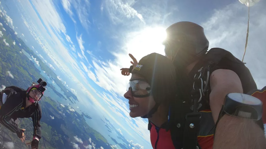 Skydivers meet midair with wide smiles and parachutes deployed over the Bay of Islands