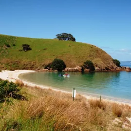 Jet skis anchored near a secluded beach surrounded by grassy hills in the Bay of Islands