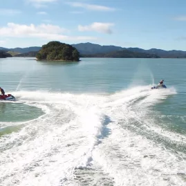 Two jet skis creating a V-shaped wake in the calm waters of the Bay of Islands