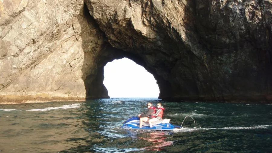 Two people on a jet ski passing by the Hole in the Rock formation in the Bay of Islands