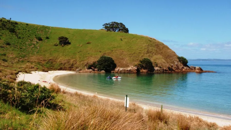 Jet skis anchored near a secluded beach surrounded by grassy hills in the Bay of Islands
