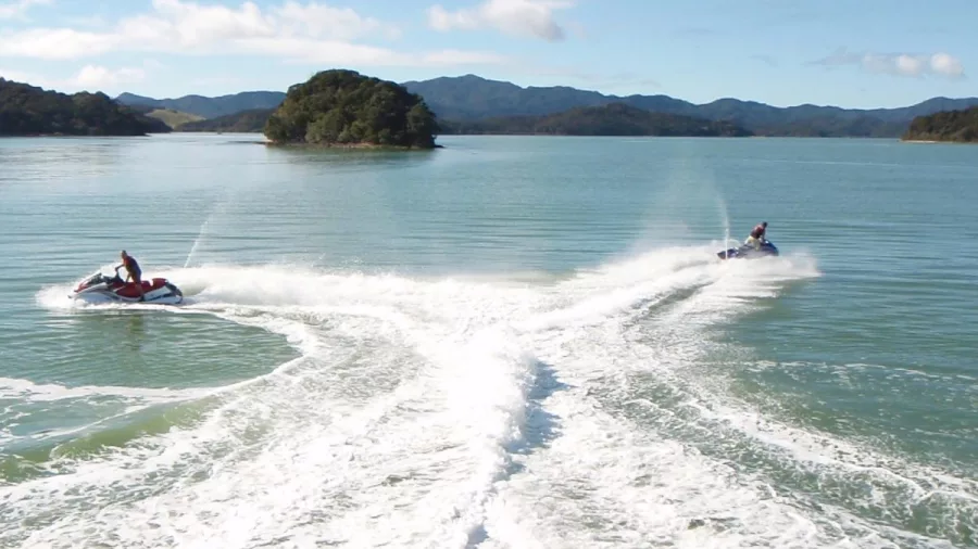 Two jet skis creating a V-shaped wake in the calm waters of the Bay of Islands