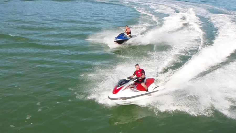 Two people riding jet skis on clear green water in the Bay of Islands