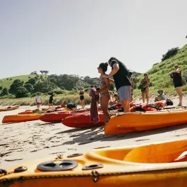 Group of kayakers preparing on a beach in the Bay of Islands during The Rock Adventure Cruise