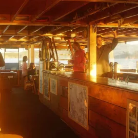 Guests relaxing on the boat deck of The Rock Adventure Cruise during golden hour in the Bay of Islands