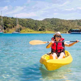 Smiling woman kayaking near The Rock boat in the Bay of Islands, New Zealand