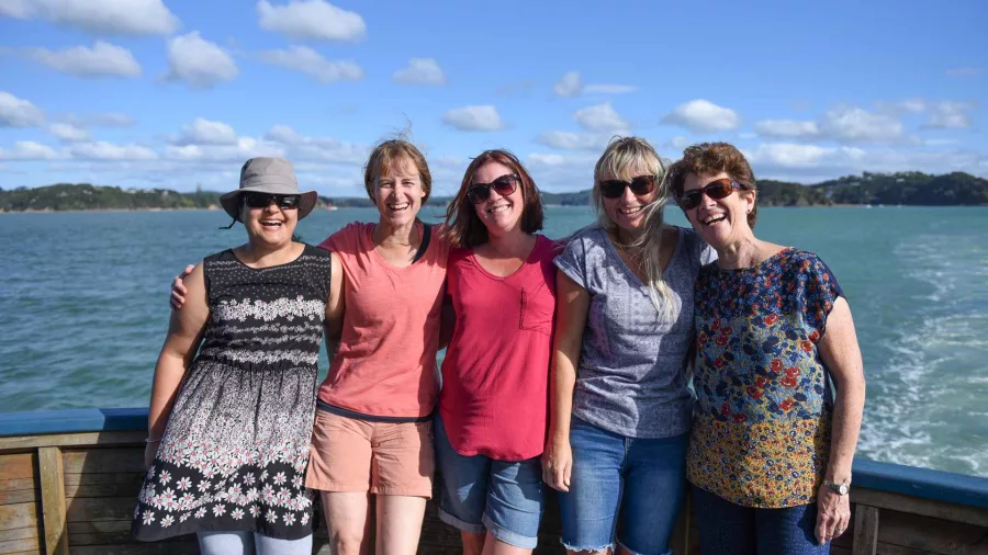 Group of smiling women posing together on the deck of The Rock Adventure Cruise in the Bay of Islands under a sunny sky